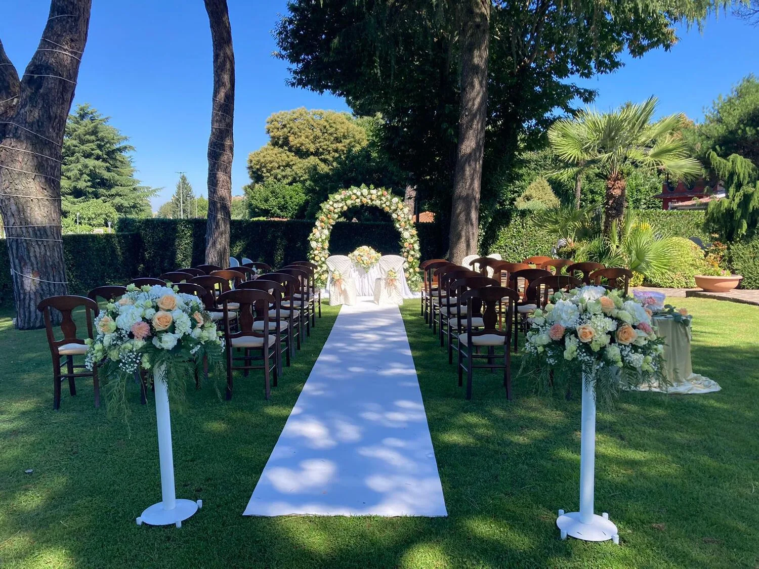 Allestimento per cerimonia all'aperto: tappeto bianco e arco di fiori nel giardino tra i pini — Le Colombe Da Tiziano
