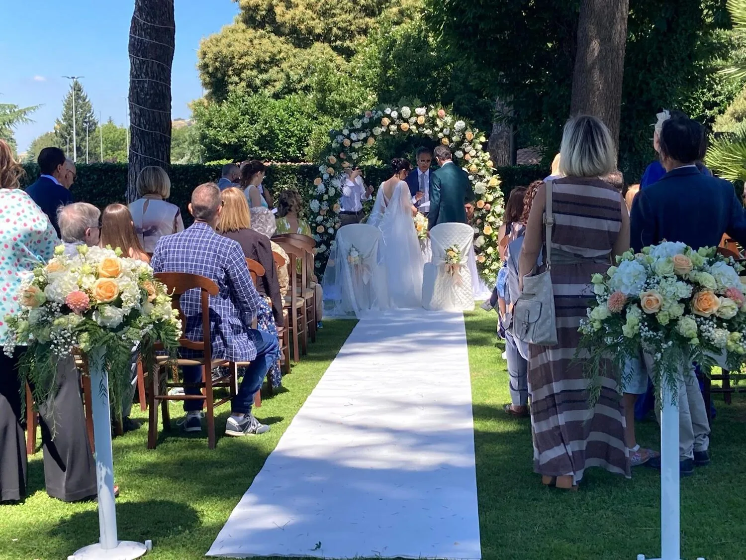 Cerimonia di matrimonio all'aperto nel giardino, sposi sotto l'arco di fiori e invitati — Le Colombe Da Tiziano